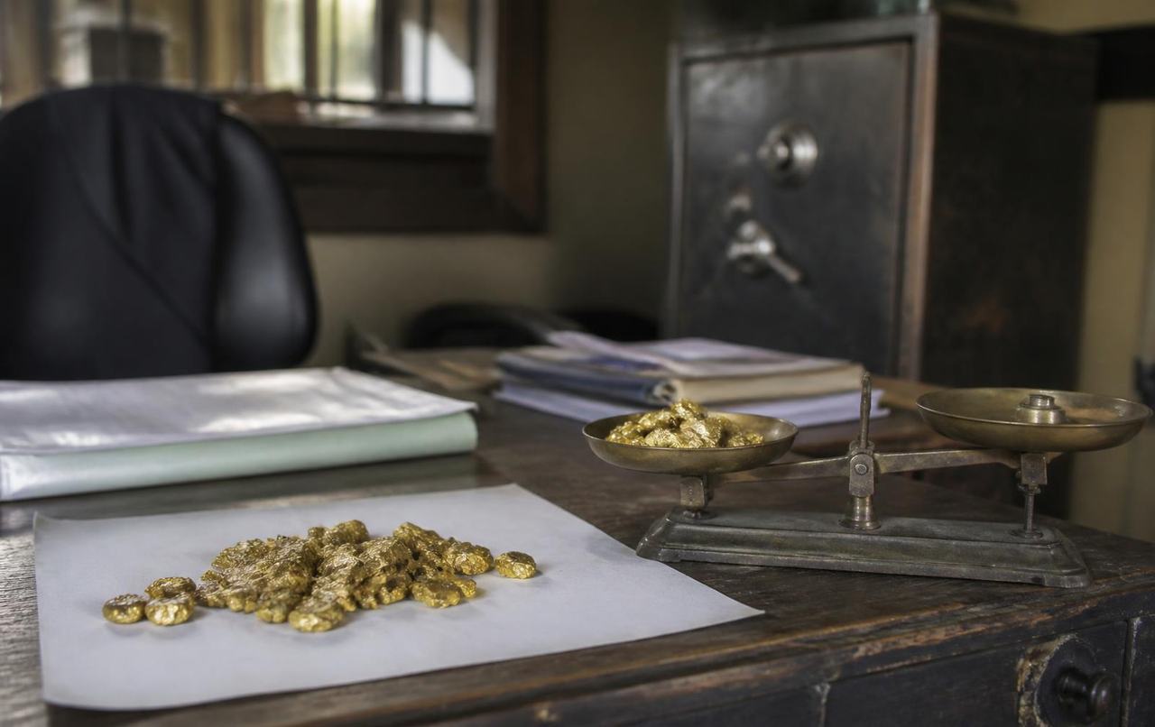 Raw gold nuggets and a brass weighing scale on a desk in a Kampala trading office